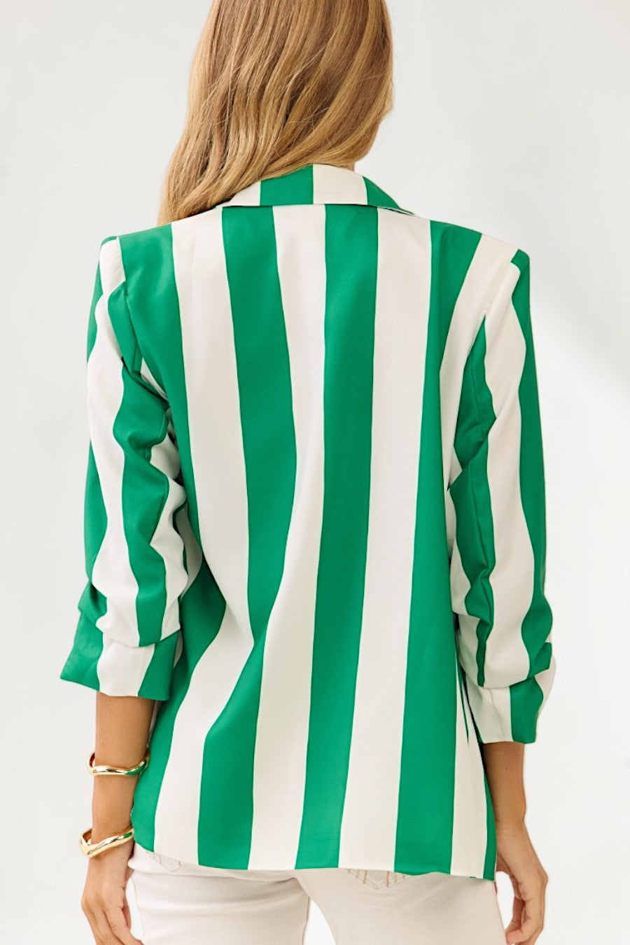 A woman shown from the back wearing a green and white vertically striped blazer with three-quarter sleeves, paired with white pants, against a plain white background.