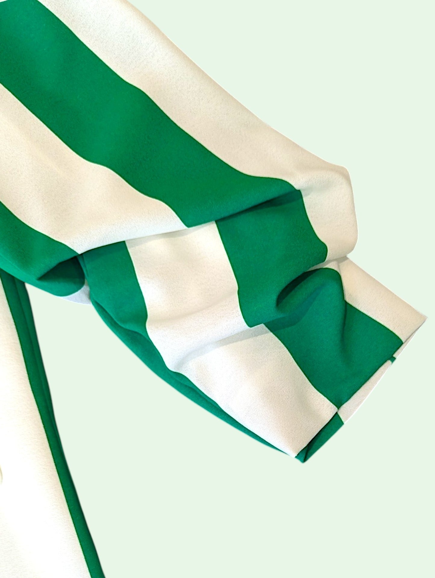A close-up of a green and white striped fabric sleeve, draped against a pale mint green background.