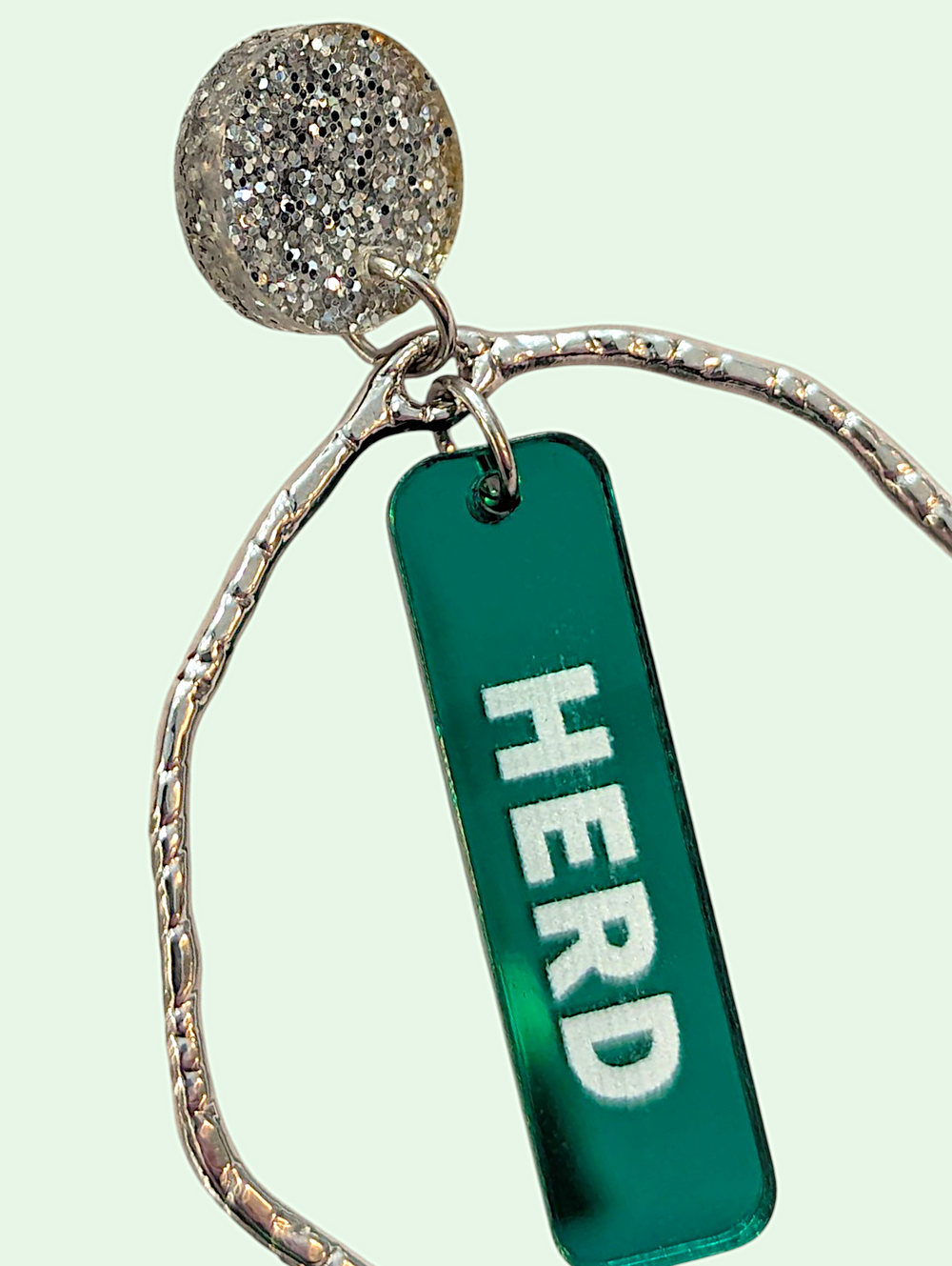 earring with green tag labeled 'HERD' on a light green background