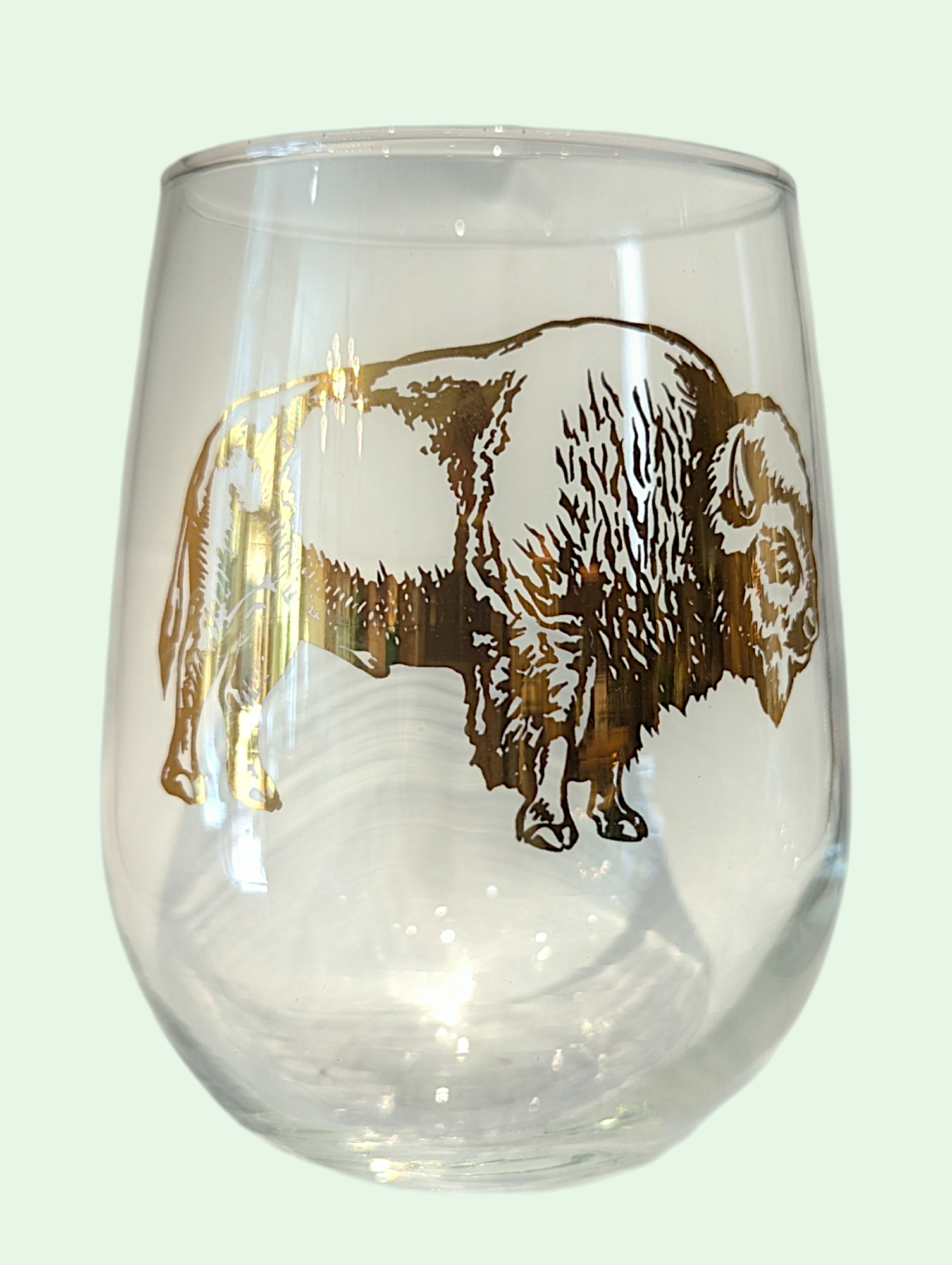 Clear wine glass with a gold bison design on a light gray background