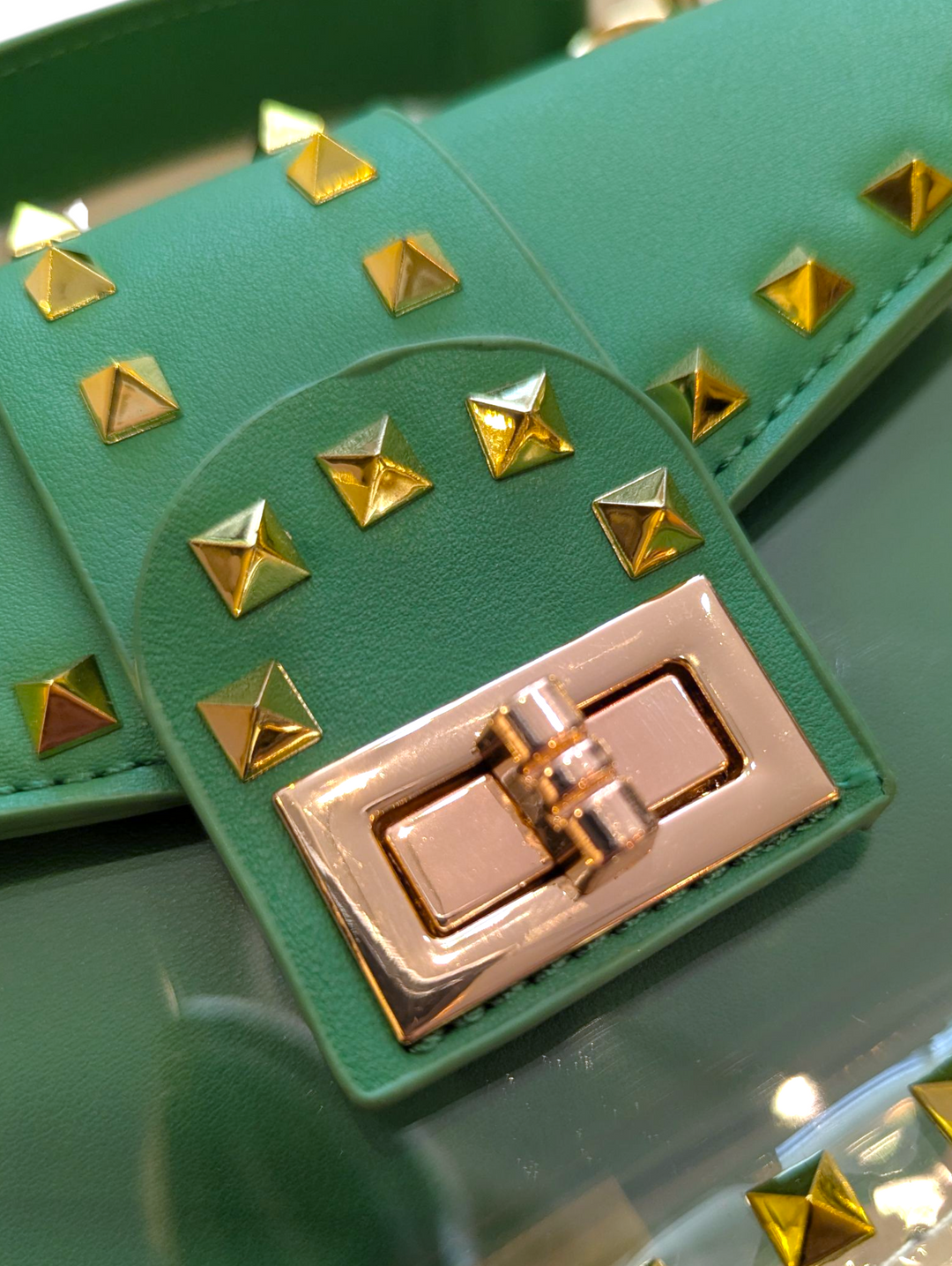 Green clutch bag with gold studs and a gold clasp on a reflective surface.