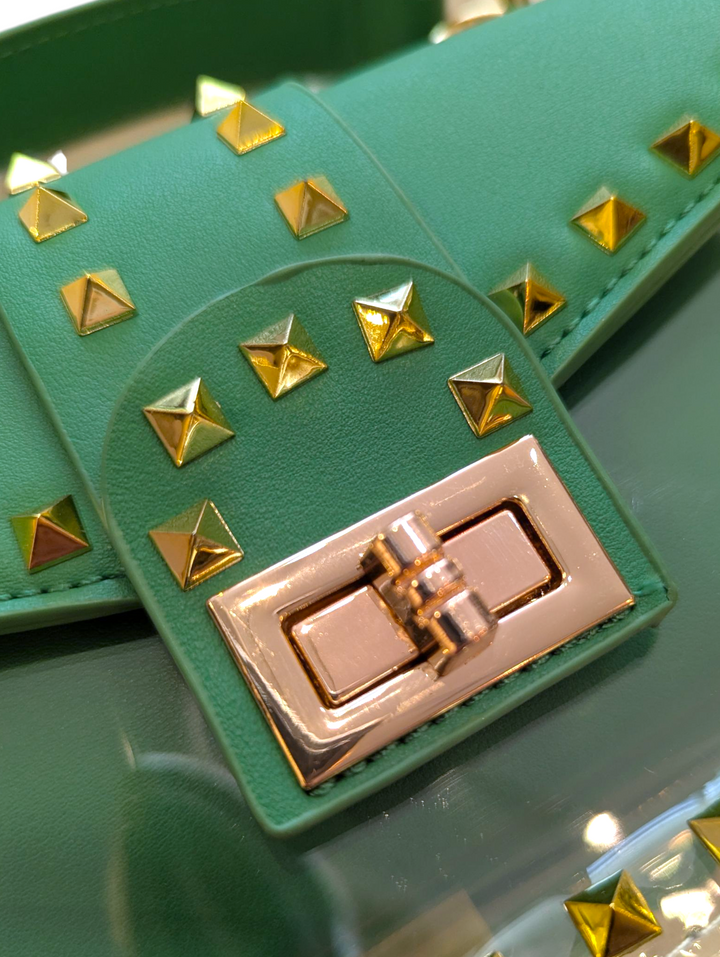 Green clutch bag with gold studs and a gold clasp on a reflective surface.