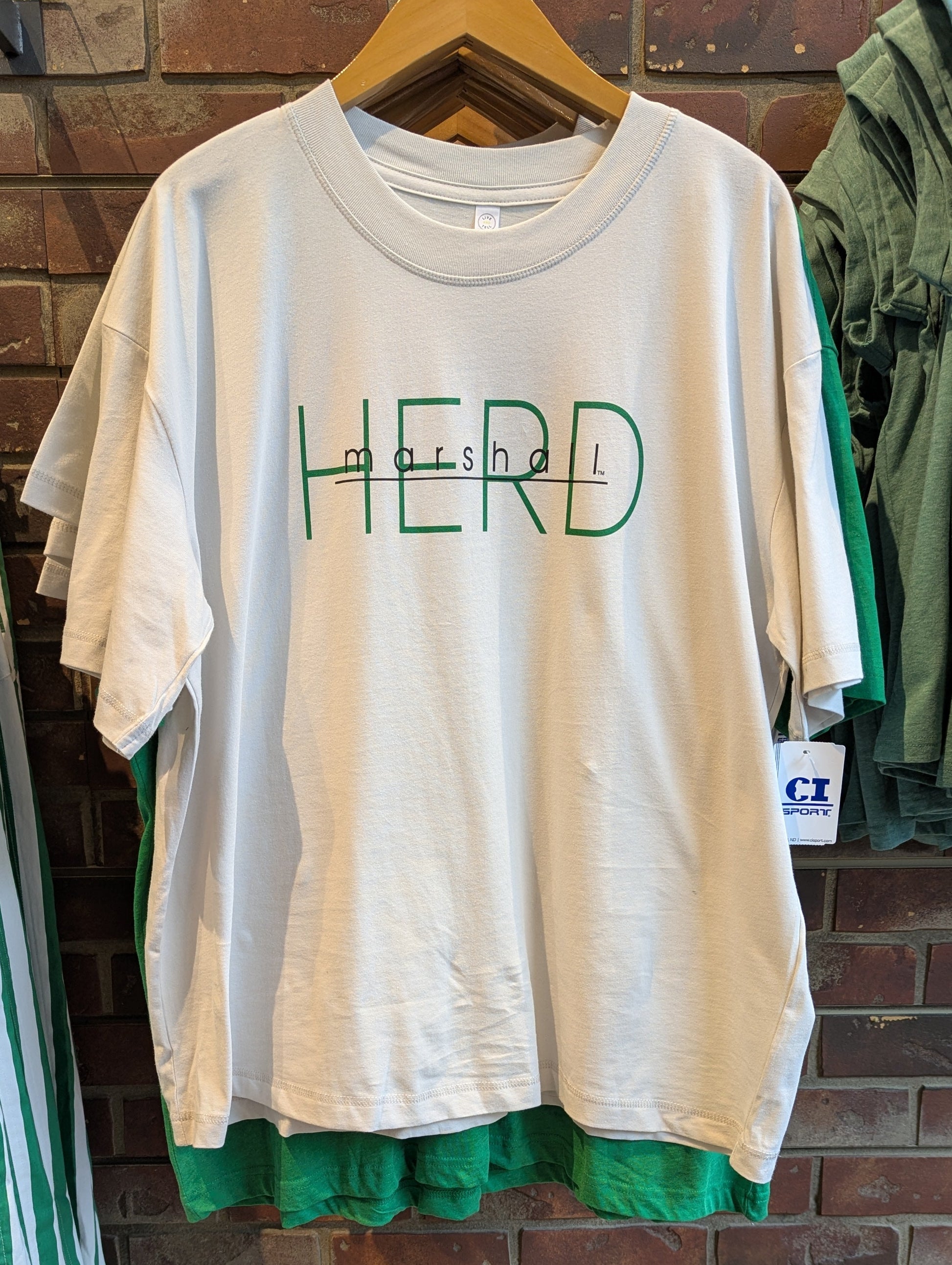 Beige t-shirt with 'HERD' printed on it hanging over a normal unisex tee to show length difference