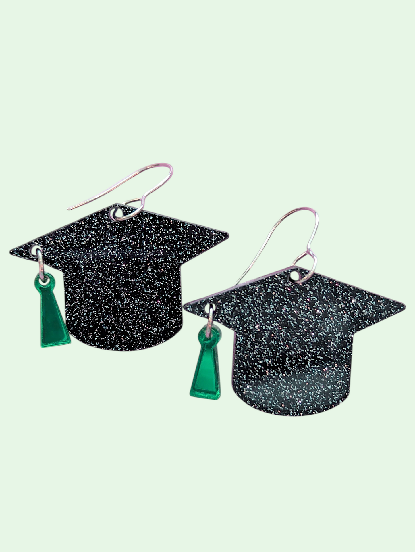 Graduation cap earrings on a light green background