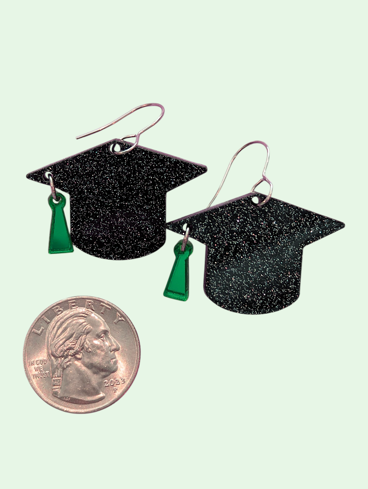 Graduation cap earrings with green tassels on a light green background