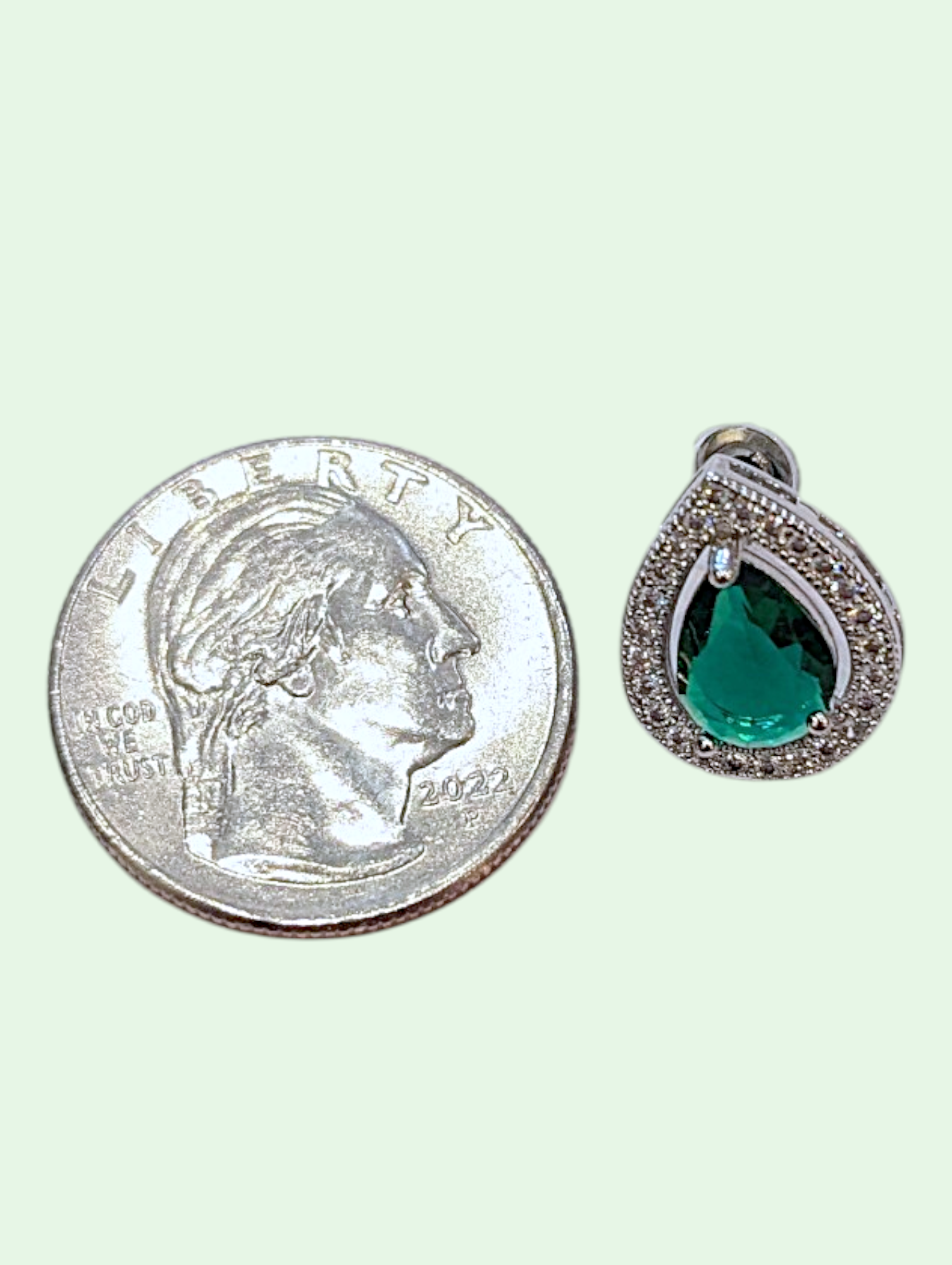 Teardrop-shaped green gemstone earring next to a quarter for size comparison on a white background