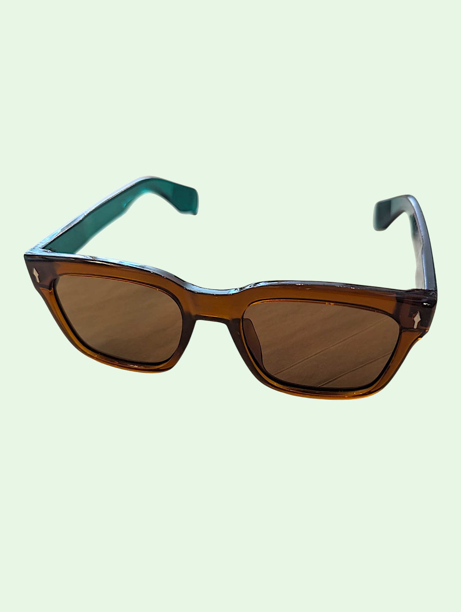 Sunglasses with brown lenses and green earpiece on a light green background