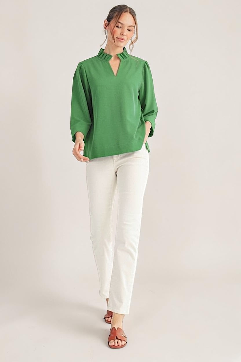 Woman wearing a green blouse and white pants on a plain background