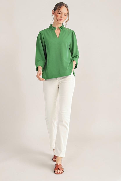 Woman wearing a green blouse and white pants on a plain background