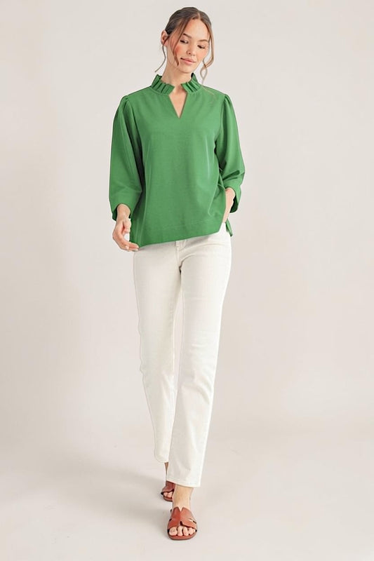 Woman wearing a green blouse and white pants on a plain background