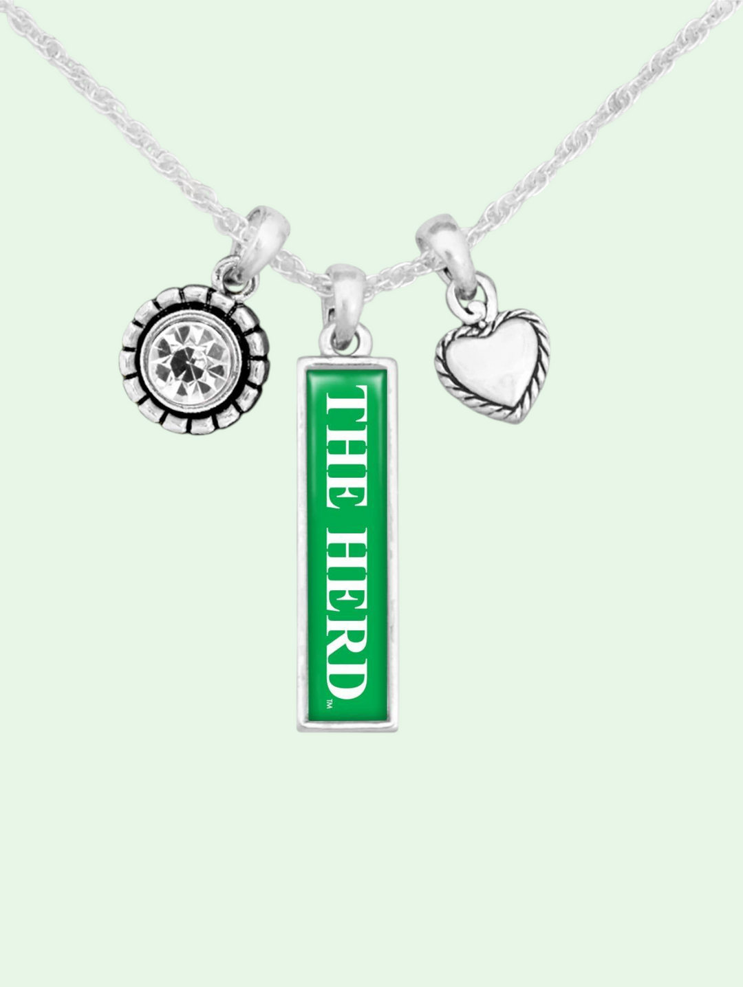 Necklace with 'The Herd' pendant, a clear jewel and a metal heart charm on a light green background