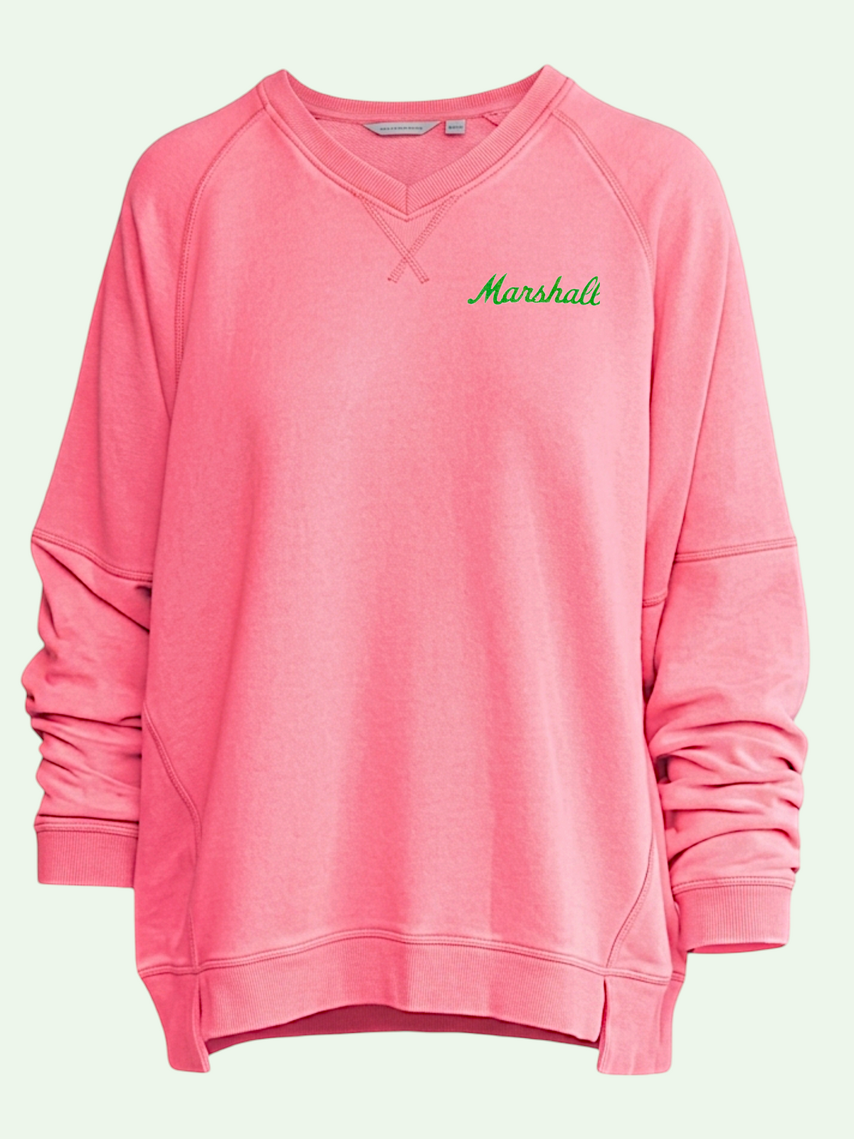 A pink long-sleeve crewneck sweatshirt with 'Marshali' printed in green script on the left chest, displayed on a solid pale green background.