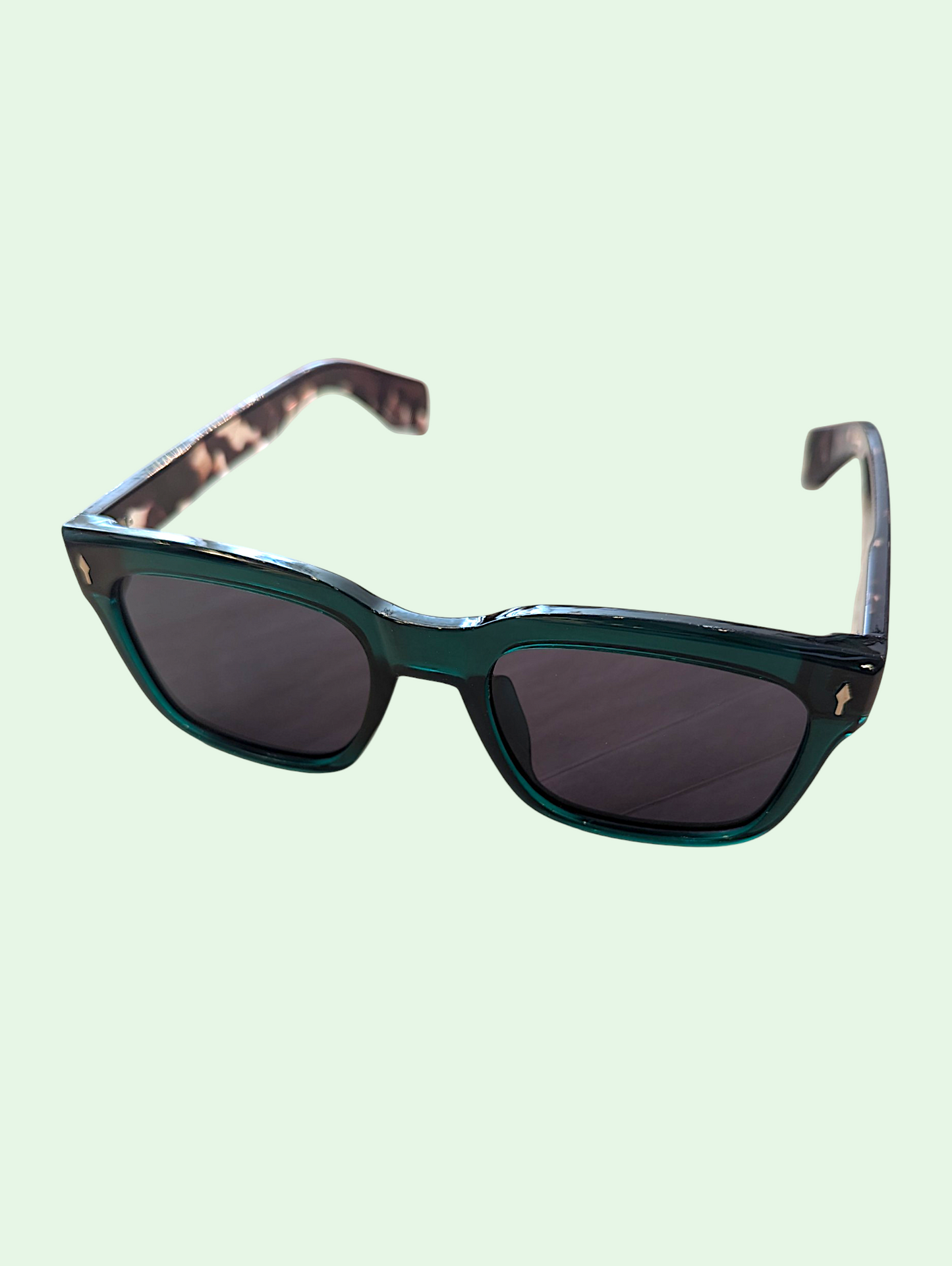 Sunglasses with a green frame and dark lenses on a light green background