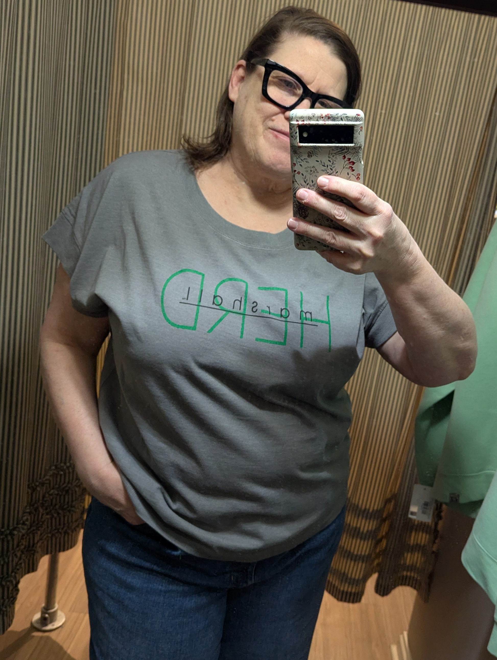 Person wearing a gray t-shirt with green text, taking a mirror selfie.