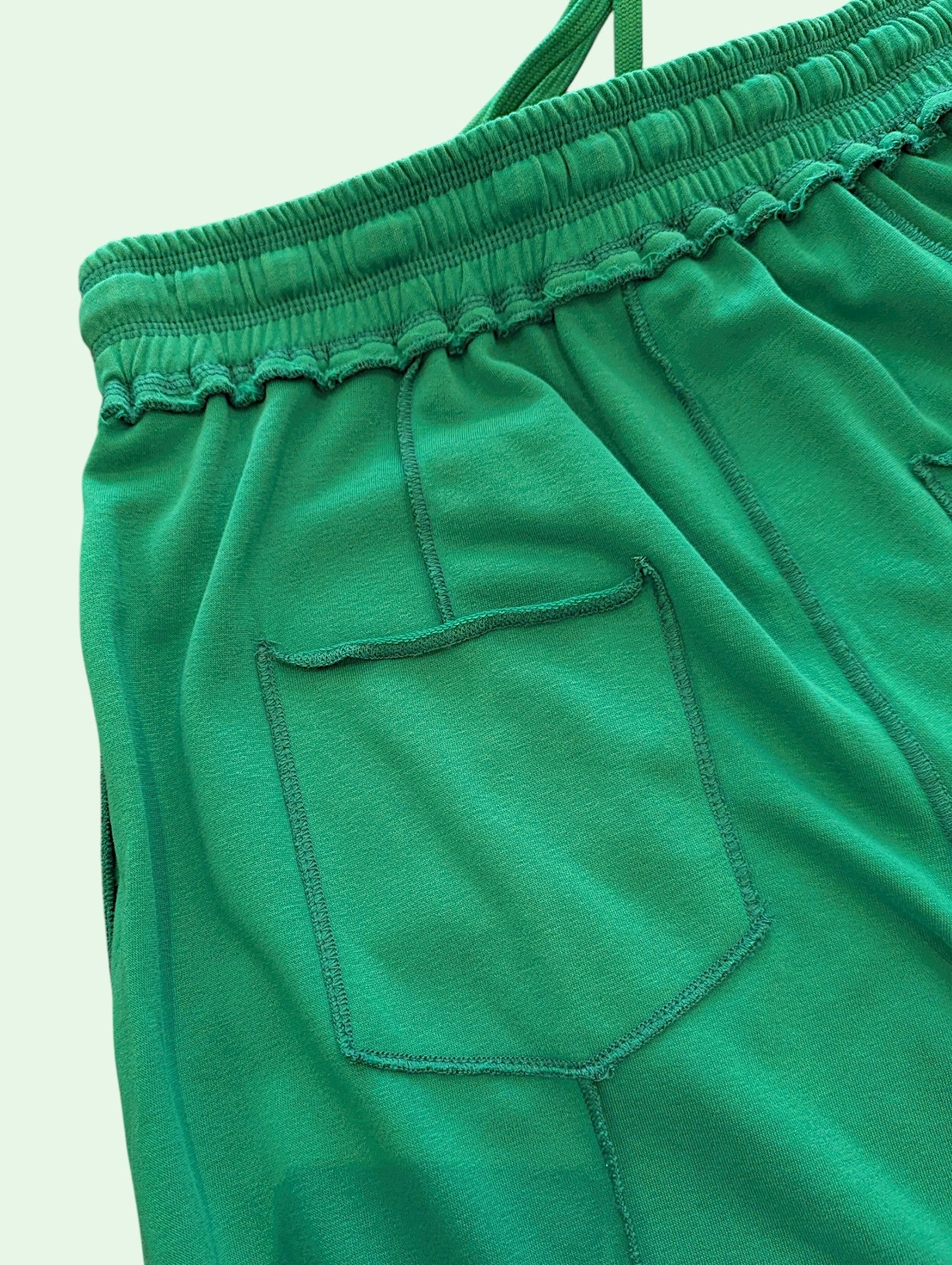 Close-up of bright green fabric with an elastic waistband and a stitched side pocket, photographed against a plain light background.