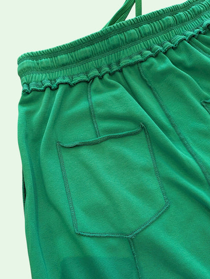Close-up of bright green fabric with an elastic waistband and a stitched side pocket, photographed against a plain light background.