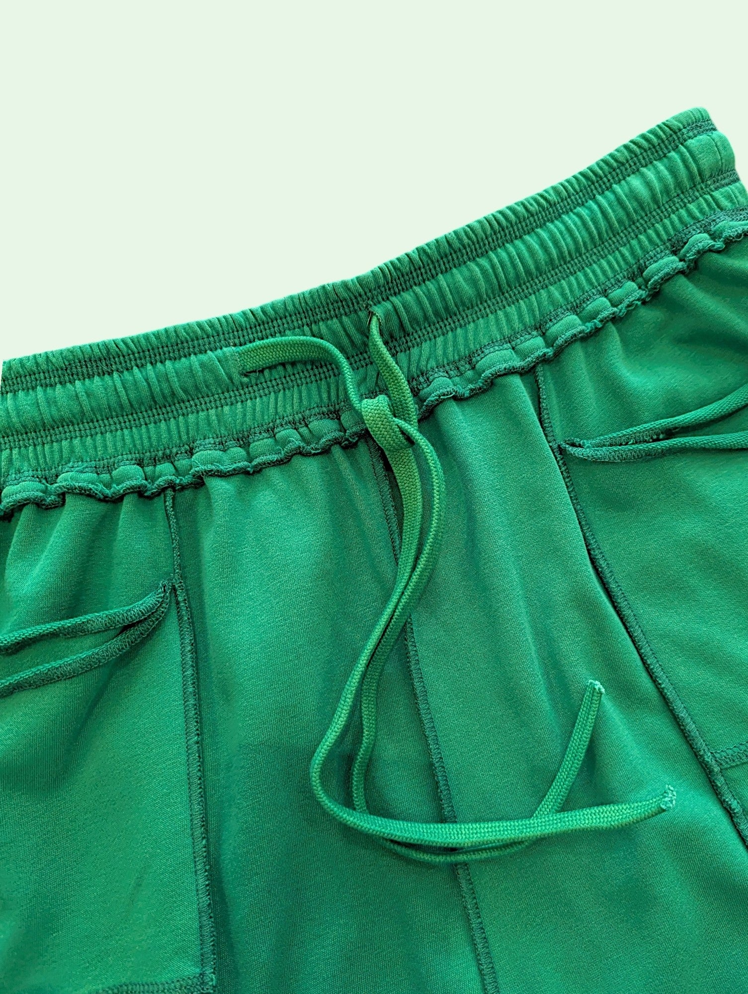 Close-up of bright green sweatpants showing the elastic waistband, matching drawstring, and side pocket details.