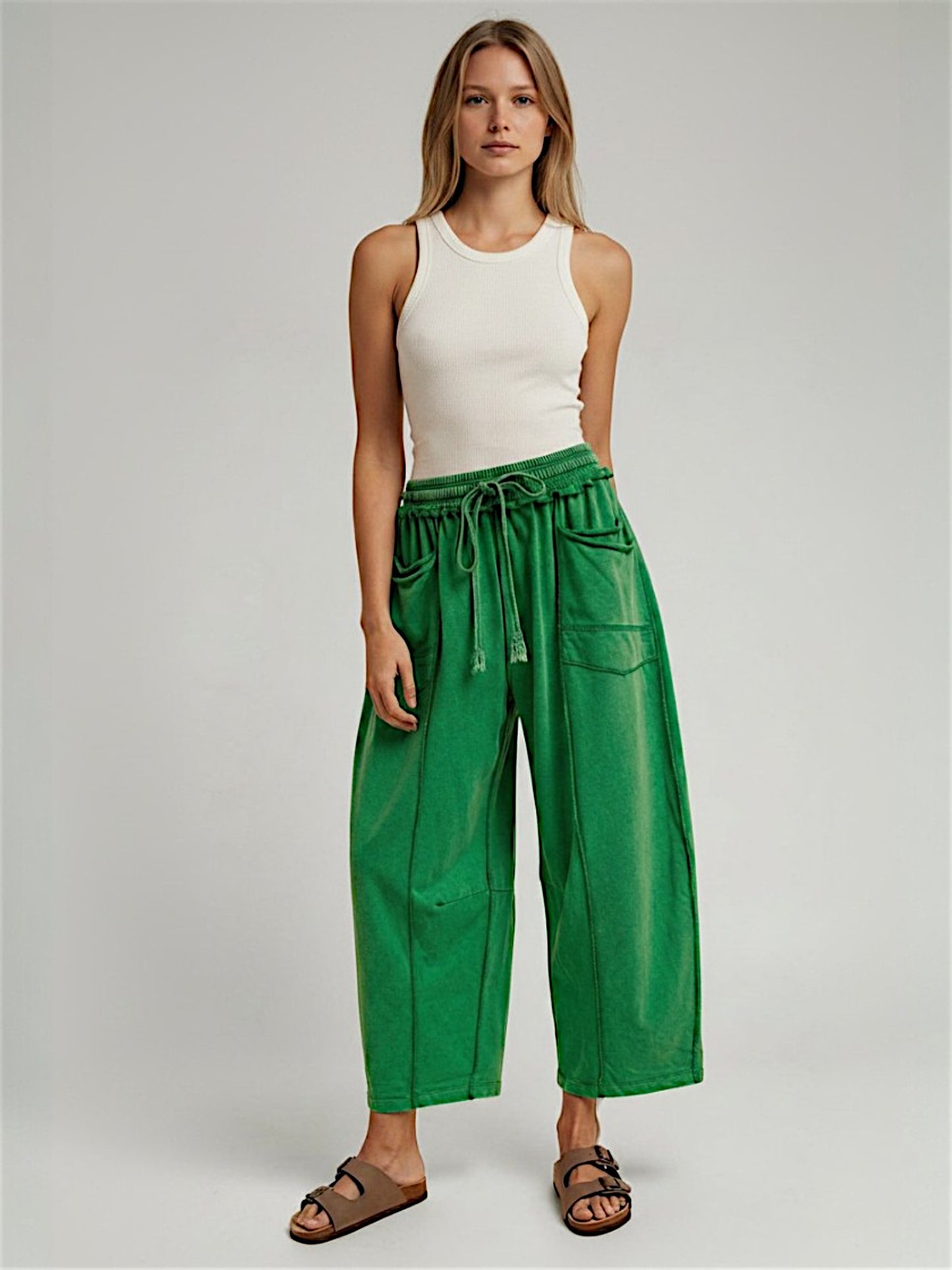 Woman wearing a white tank top and green pants on a plain background