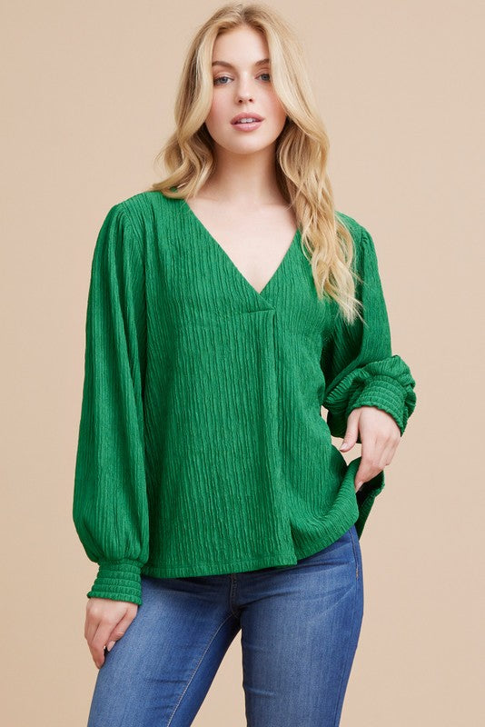 a blonde model stands facing the camera, hand on hip, showing us the textured top. it has long sleeves and a vneck.