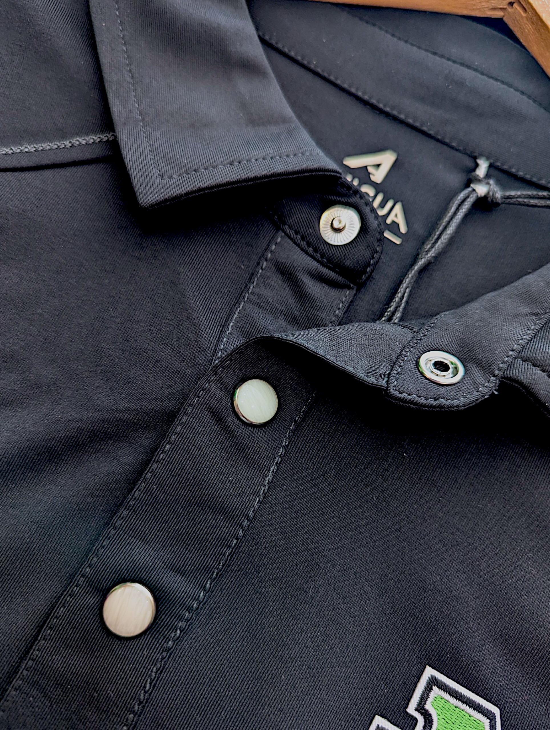 Close-up of a black polo with buttons and a brand logo.