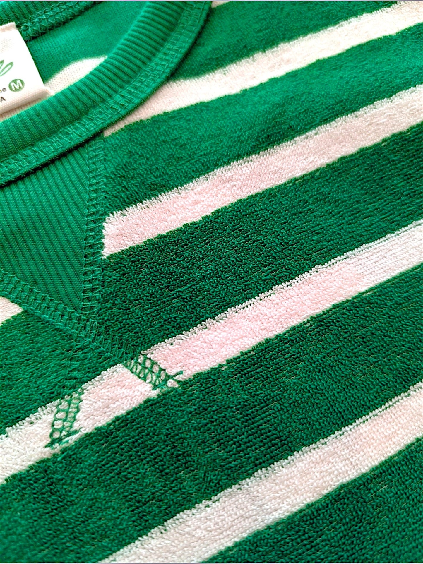 Close-up of a green and white striped knit garment, showing the textured fabric, ribbed collar, and part of a white inner tag.