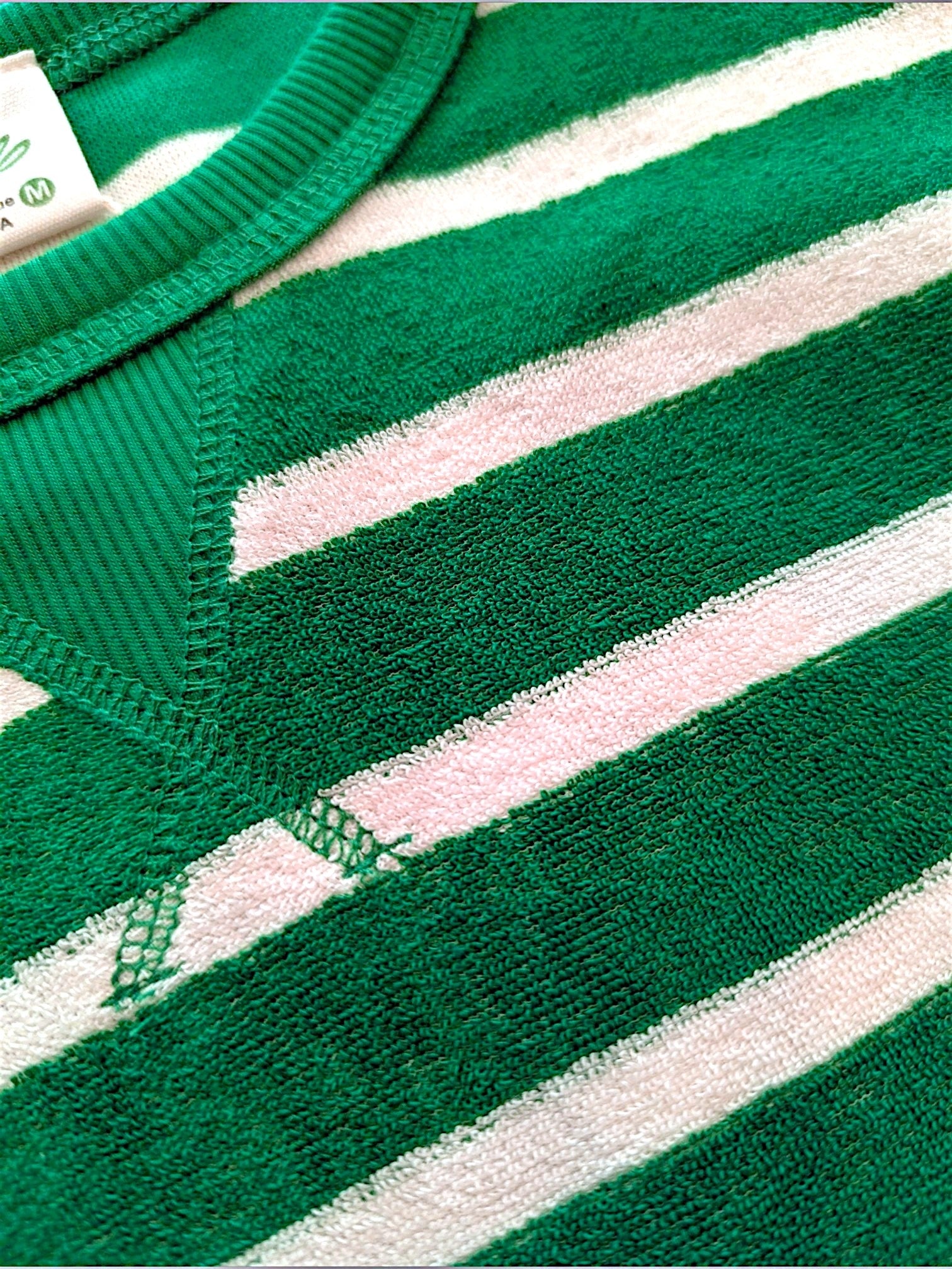 Close-up of a green and white striped knit garment, showing the textured fabric, ribbed collar, and part of a white inner tag.