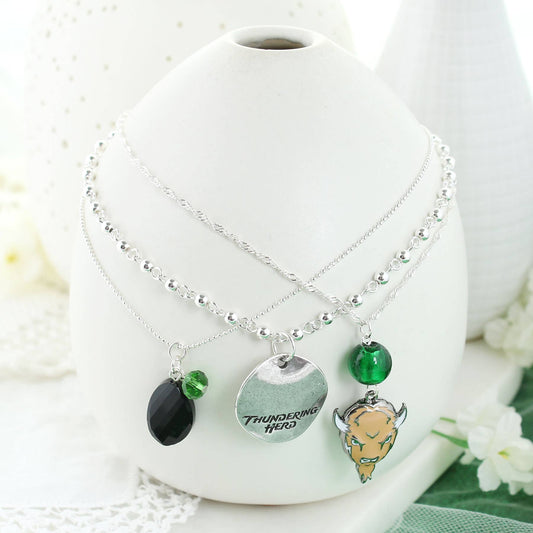 Set of three silver plated 16” necklaces (each with a claw clasp and 3” extender). Each necklace features a different chain style and charm, to include green and black beads, an enamel Marshall logo charm, and a silver stamped disc featuring the “Thundering Herd” slogan. On white vase