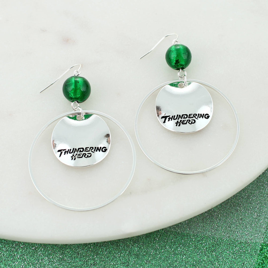 Silver plated shepherd hook earrings featuring a dangling “Thundering Herd" slogan disc with a green bead accent and silver plated hoop. On white background